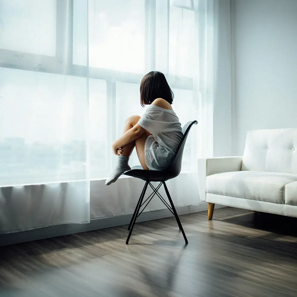Personne assise près d’une fenêtre, les genoux repliés